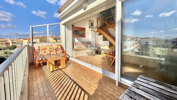 A balcony with a wooden table, chairs, and a sofa. There is a staircase leading to an upper floor. - CAP D'AGDE - Plage Richelieu / Réf 0156 (CAP D'AGDE)