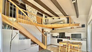 A spacious living area with a wooden staircase, a dining table, and a kitchen area. - CAP D'AGDE - Plage Richelieu / Réf 0156 (CAP D'AGDE)