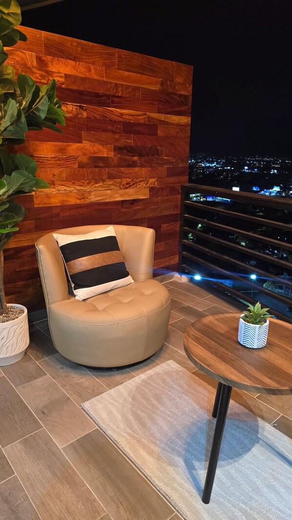 Un espace extérieur moderne aménagé avec un mur en bois, un fauteuil rembourré avec un coussin à rayures, une table en verre et une plante en pot.