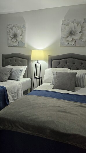 Ein Hotelzimmer mit zwei Betten, einer Stehlampe und Blumenbildern an der Wand.