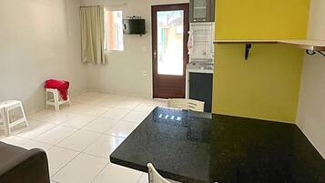 Um quarto com uma mesa preta e cadeiras brancas, um banquinho pequeno com um pano vermelho, um sofá branco e uma parede amarela.