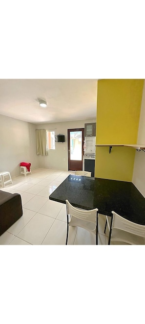 Una habitación con una mesa negra y sillas blancas, un taburete pequeño con tela roja, un sofá blanco y una pared amarilla.