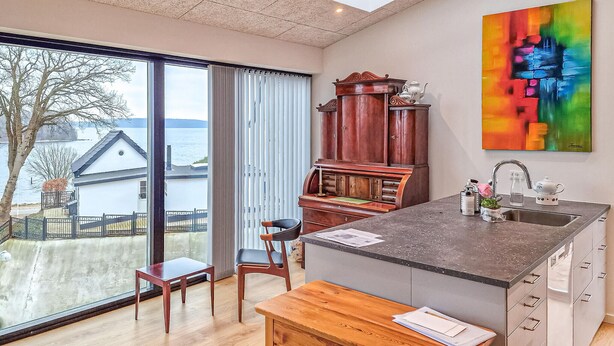 Une cuisine moderne dotée d’un grand îlot central, d’un meuble en bois et d’un tableau abstrait aux couleurs vives accroché au mur.