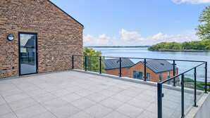 Un bâtiment moderne avec une façade en briques et une porte en verre, donnant sur une étendue d’eau paisible et une végétation luxuriante.