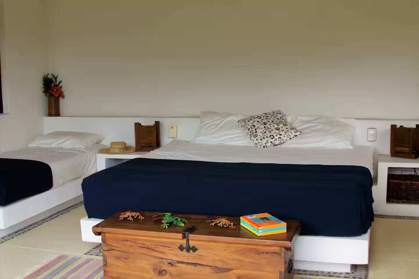 A hotel room with two single beds, a wooden chest, and a small table with a book and decorative items.