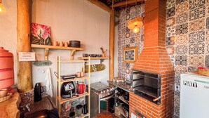 A compact kitchen with a brick oven, wooden shelves, and patterned tiles. - Pousada Reserva Setiba (Guarapari)