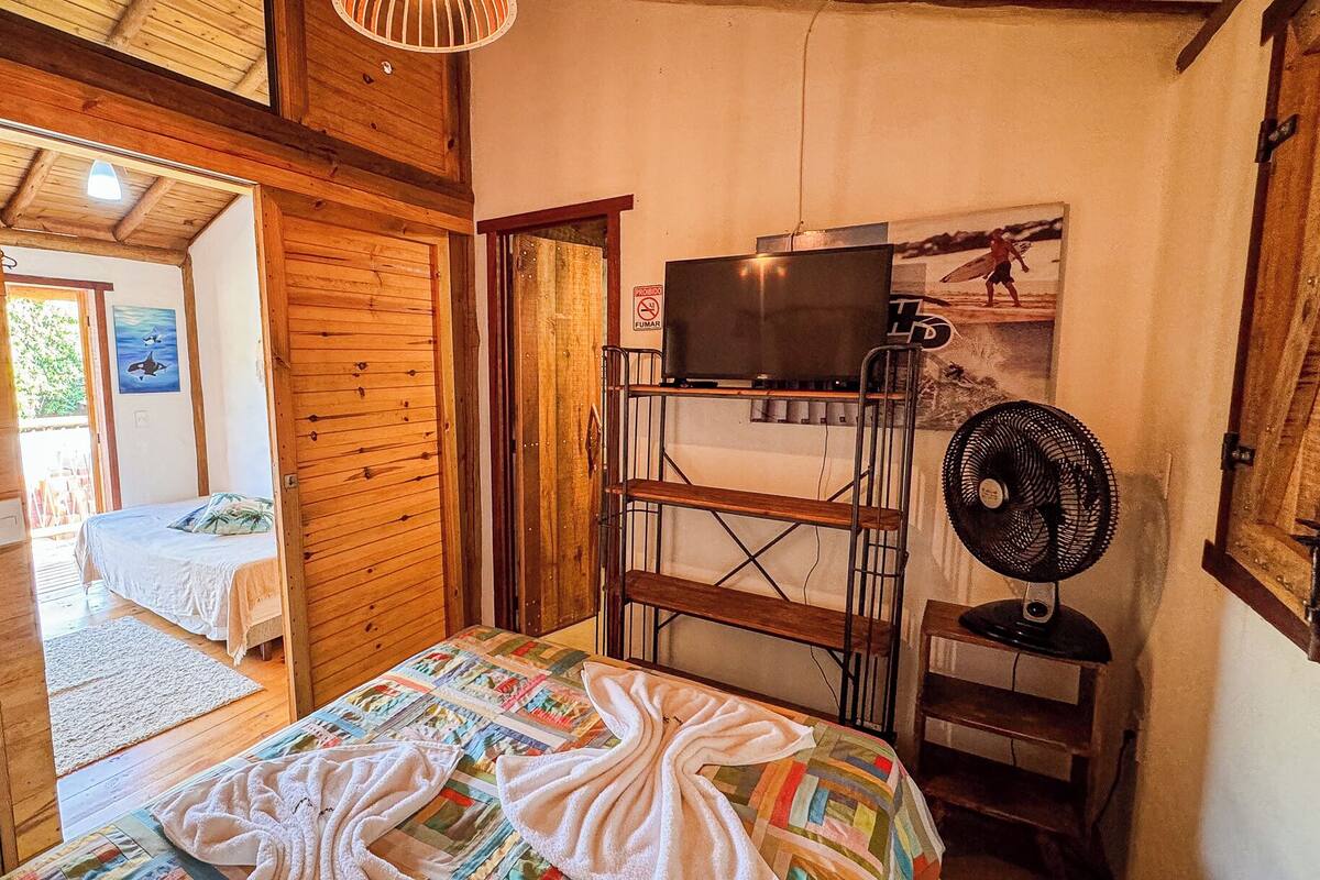 Una habitació de fusta amb un llit superposat, una televisió sobre una estant i un ventilador.