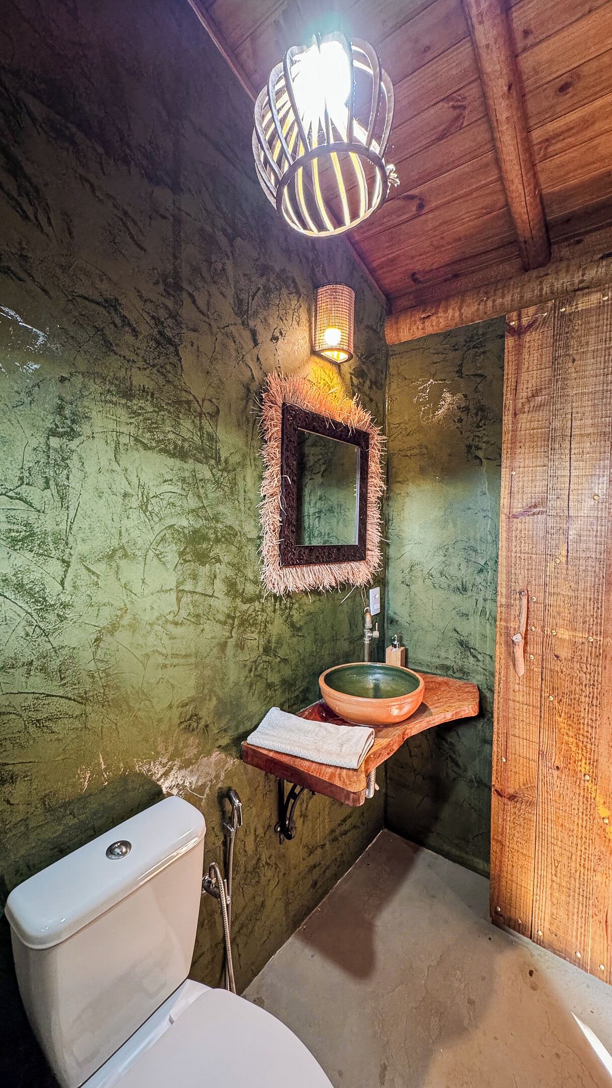 A rustic bathroom with a wooden sink, a toilet, a mirror, and a hanging light fixture.