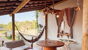 A wooden deck with a hammock, a round wooden table, and a sofa. - Pousada Reserva Setiba (Guarapari)