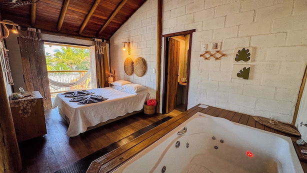 A room with a bed, a wooden floor, a white wall, a wooden ceiling, a window, and a jacuzzi. - Pousada Reserva Setiba (Guarapari)