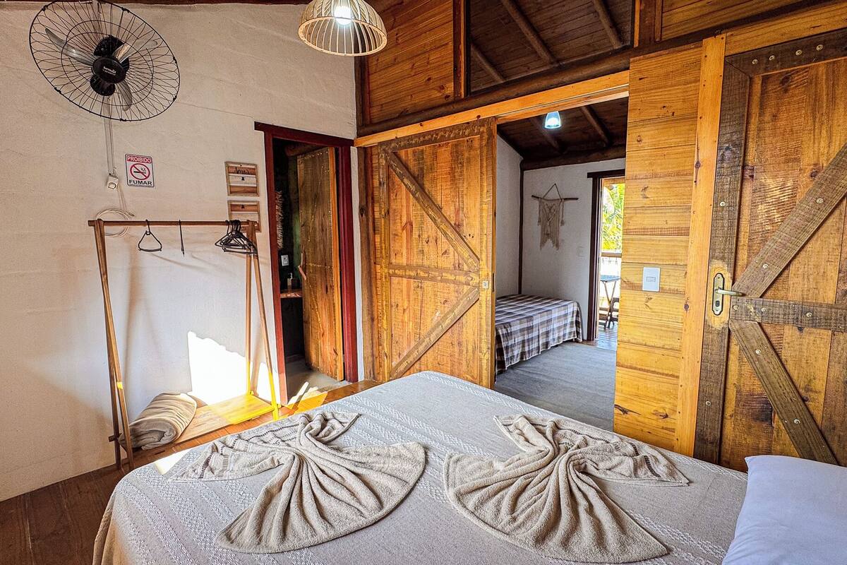 Habitació rústica amb un llit, portes de fusta i un ventilador.