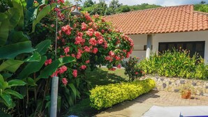A house with a tiled roof, a garden with pink flowers, and a swimming pool.