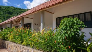 A building with a tiled roof, stone walls, and a garden with tropical plants.