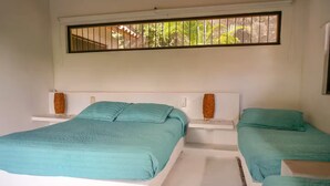A bedroom with two beds, white headboards, and a window with a view of greenery.
