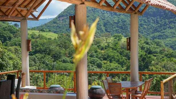 A wooden gazebo with a table and chairs, overlooking a lush green landscape.