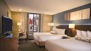 A hotel room with two beds, a desk with a TV, and a window with a city view.