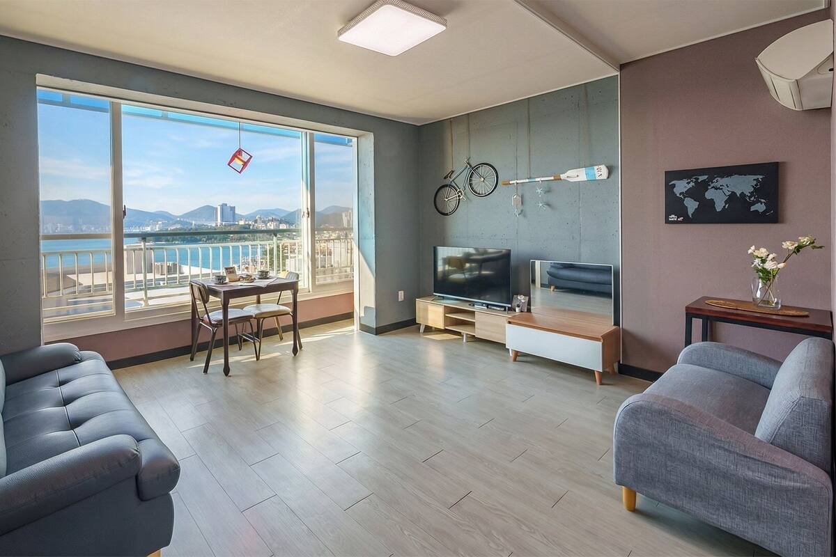 A modern living room with a large window, a sofa, a TV, and a dining area.