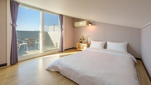 Habitación de hotel con una cama grande, una mesita de noche, una lámpara y vista al mar a través de una puerta corrediza de vidrio.