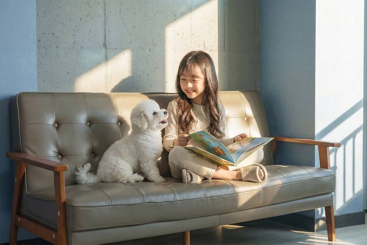 A person sitting on a sofa with a dog, reading a book.