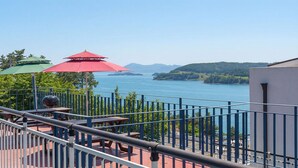 Un balcón con mobiliario exterior, una parrilla y vistas a un lago y colinas.