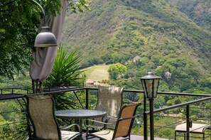 A terrace with a table and chairs, overlooking a lush valley with a mountain in the background.