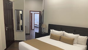 Un letto rifatto con biancheria bianca e beige, una testiera scura e un comodino con una lampada.