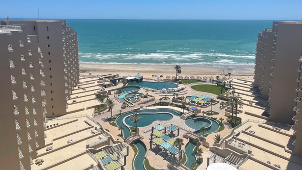 Un resort con diverse piscine, una spiaggia e alti edifici.