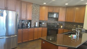 Una cucina moderna con mobili in legno, elettrodomestici in acciaio inossidabile, un piano di lavoro in granito e una parete rivestita in piastrelle.