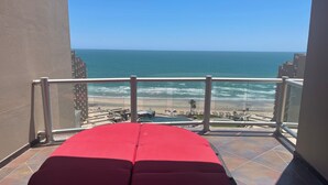 Un balcone con una zona relax imbottita di rosso, con vista sulla spiaggia e sull'oceano.