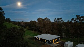 A modern house with a flat roof, surrounded by trees and a grassy hill. - Nannup Bush Retreat · Firepit, Walk to Town (Nannup)