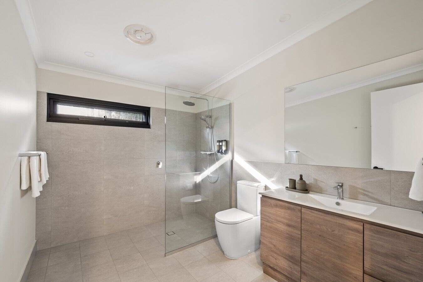 A modern bathroom with a glass-enclosed shower, a toilet, and a vanity with a mirror.