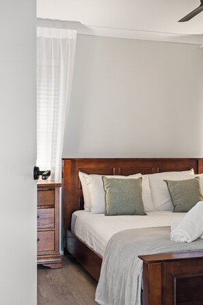 A bedroom with a wooden headboard, a bed with white bedding, a wooden nightstand, and a white curtain. - Nannup Bush Retreat · Firepit, Walk to Town (Nannup)