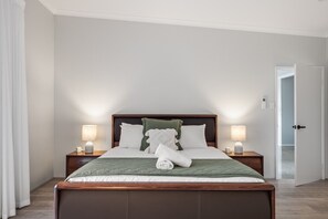 A hotel room with a bed, two bedside tables with lamps, a door, and a view of the hallway.