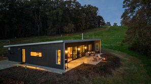 A modern house with a large glass door, a fire pit, and a well-maintained lawn.