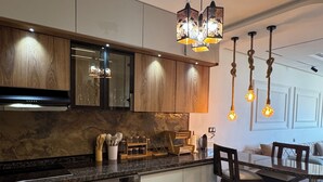 Een moderne keuken met een inbouwoven, wasmachine en houten kasten. Er is een eethoek met een tafel en stoelen.