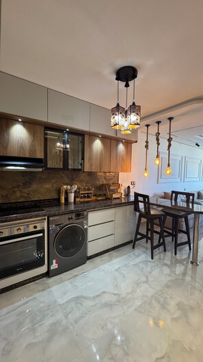 A modern kitchen with a built-in oven, washing machine, and wooden cabinets. There is a dining area with a table and chairs. - Sea View | Telescope | Lux Apart | Malabata Beach | TGV | Tangier City Mall (Tanger)