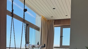 Een moderne kamer met grote ramen, een telescoop, een macramé stoel, een houten tafel en een potplant.