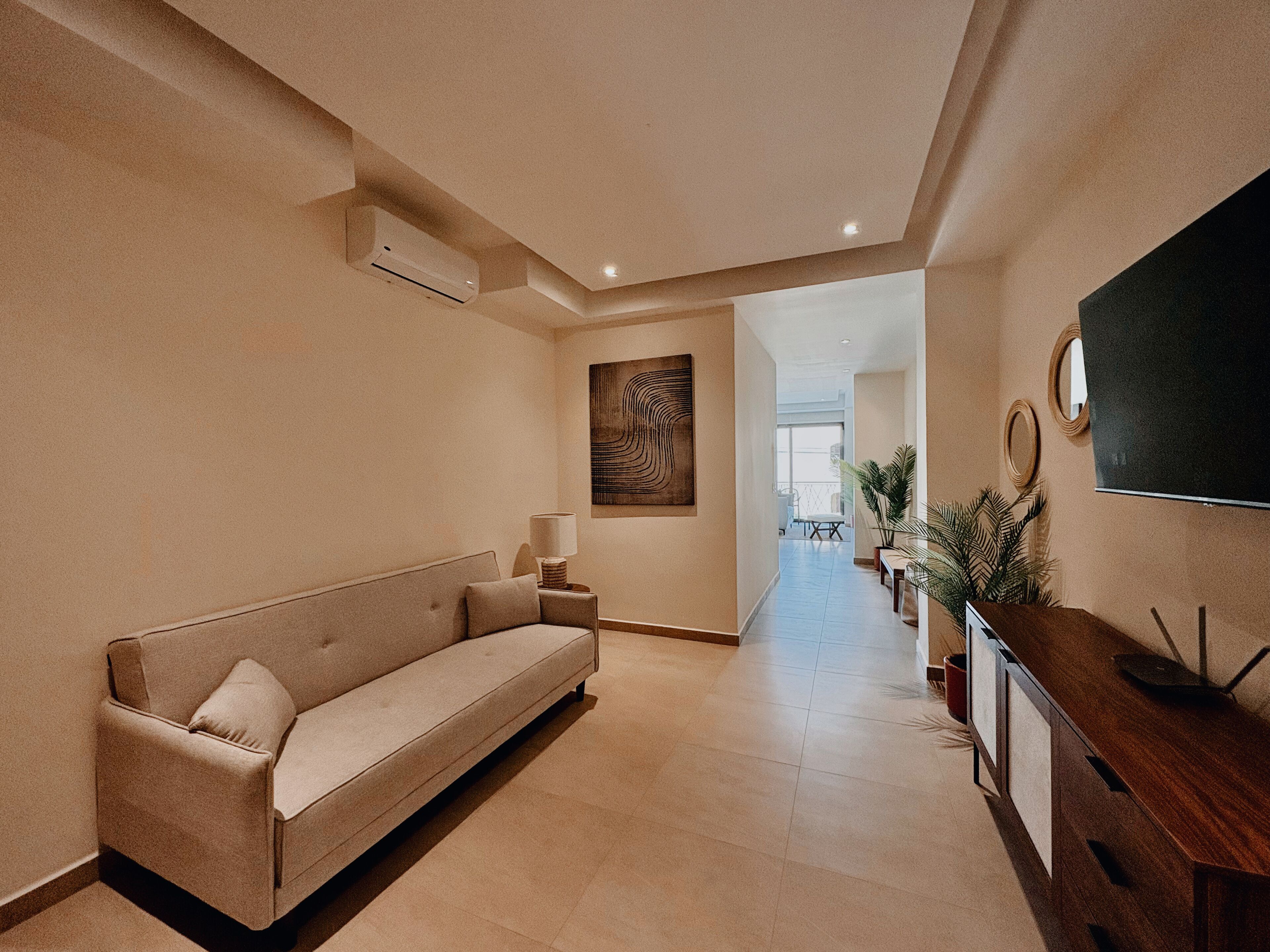 A modern hotel lobby with a sofa, a TV, and a wooden console.
