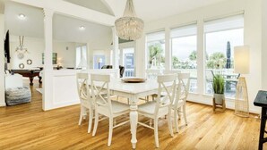 Una cocina amplia con una mesa y sillas blancas, ventanas grandes y una araña.