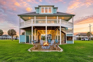 A two-story house with a balcony, a fire pit, and outdoor seating. - Crystal Beach | 5BR | Ocean View + Fire Pit (Bolivar Peninsula)