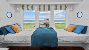 Ein Zimmer mit zwei Betten und Blick auf einen Strand durch ein großes Fenster.