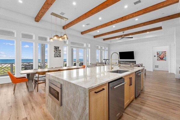 A spacious kitchen with a large island, wooden beams, and a view of the ocean. - Beachfront + Hot Tub | Game Room + Pets | Sleep 18 (Galveston)