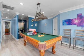 A pool table in a room with blue walls, a ceiling fan, and a painting. - Galveston Canal Home | Large Deck | Sleeps 14 (Galveston)