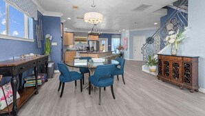 A spacious living area with a dining table, blue chairs, a chandelier, and a staircase with decorative railings.