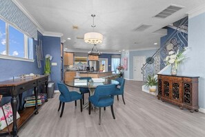 Un vaste espace de vie comprenant une table à manger, des chaises bleues, un lustre et un escalier agrémenté de rampes décoratives.