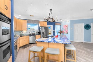 A modern kitchen with a central island, stainless steel appliances, and a blue and white backsplash. - Galveston Canal Home | Large Deck | Sleeps 14 (Galveston)