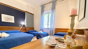 A hotel room with two single beds, a wooden table with a tray of items, a window with curtains, and a framed picture on the wall. - Hotel Praja Mare (Praia a Mare)