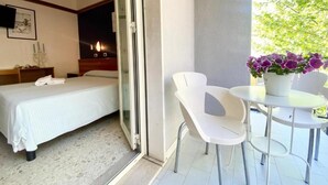 A hotel room with a bed, a small table with chairs, a potted plant, and a sliding glass door leading to a balcony. - Hotel Praja Mare (Praia a Mare)