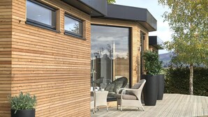 A modern house with a wooden exterior, large sliding glass doors, a deck with outdoor furniture, and a view of the landscape. - Fishmore Hall Hotel and Boutique Spa (Ludlow)