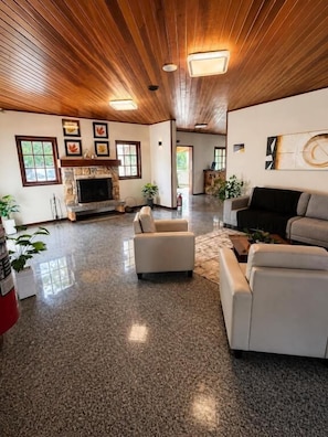 A spacious living room with a fireplace, two sofas, and a large window. - Pousada Chateau Elegance (Campos do Jordão)